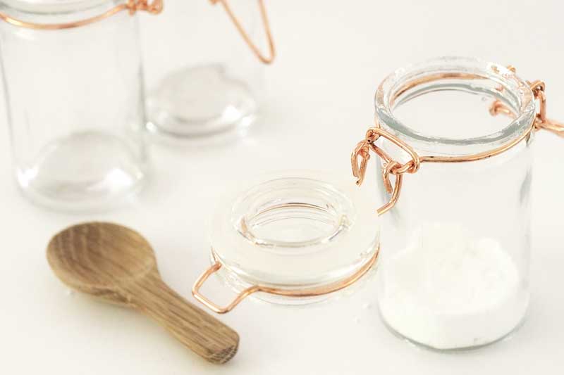 glass jar of white sugar next to wooden spoon