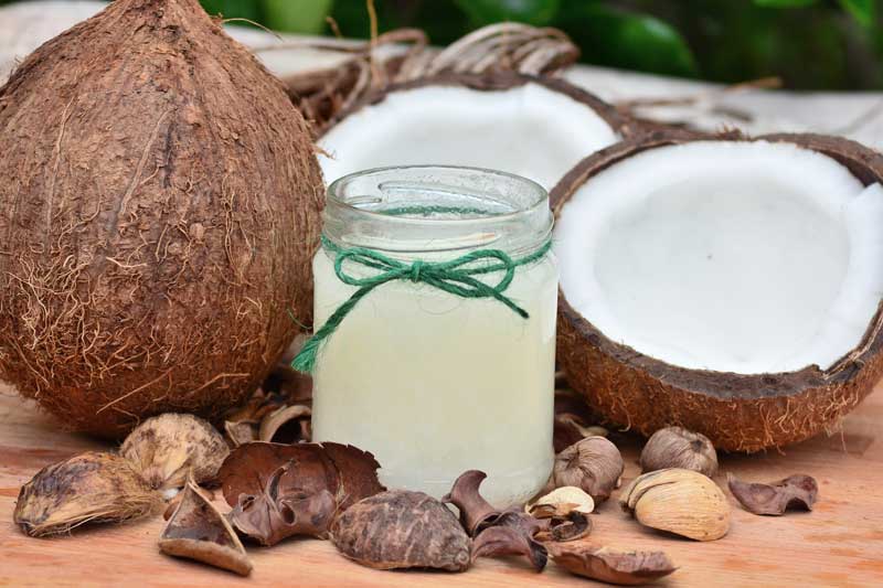 open jar of coconut oil next to a whole coconut and a coconut cracked in half