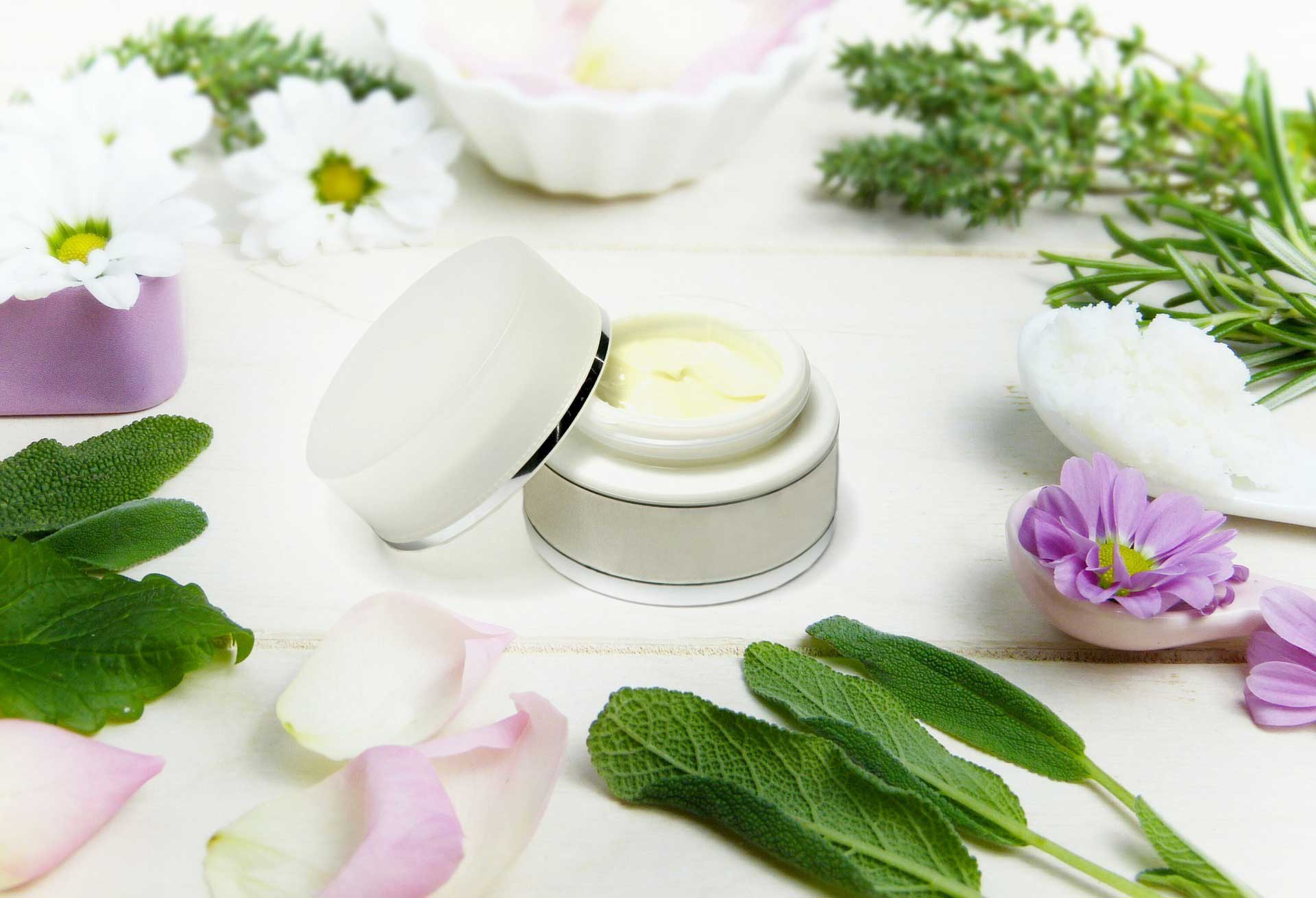 white cosmetics jar full of cream with lid off surrounded by leaves and flowers