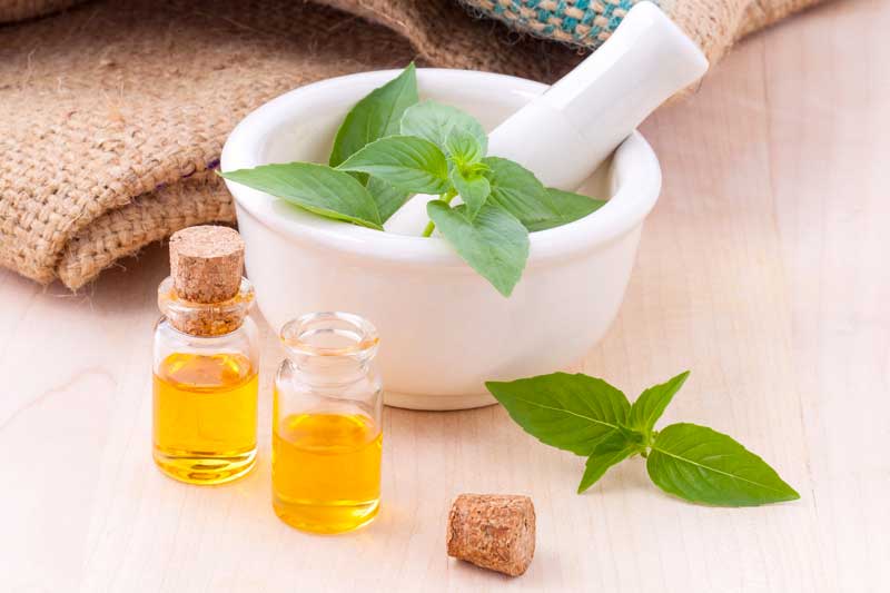 white pestle and mortar with green leaves next to two very small corked jars of oil